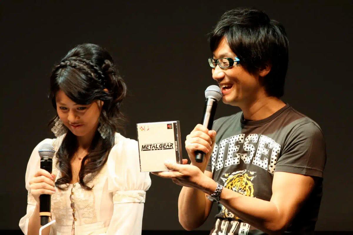 Hideo Kojima ținând carcasa unui joc Metal Gear în timp ce vorbește la un microfon.